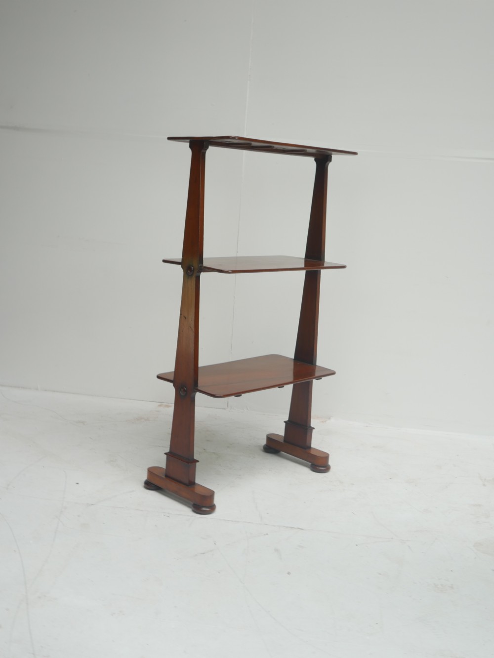 A 19th-century warm brown mahogany whatnot shelf unit featuring three open rectangular tiers supported by tapered upright side panels resting on trestle feet. View XIII