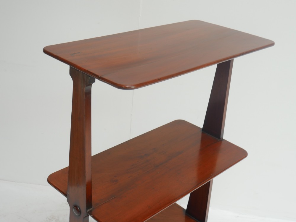 A 19th-century warm brown mahogany whatnot shelf unit featuring three open rectangular tiers supported by tapered upright side panels resting on trestle feet. View VI