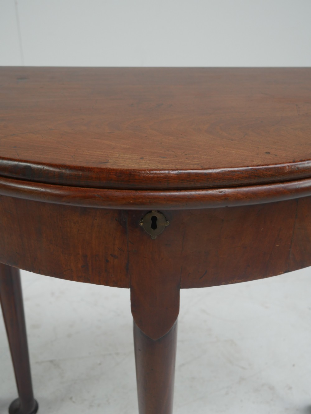 An 18th-century mahogany demi-lune games table featuring a folding semi-circular top supported by slender legs with pad feet. View V