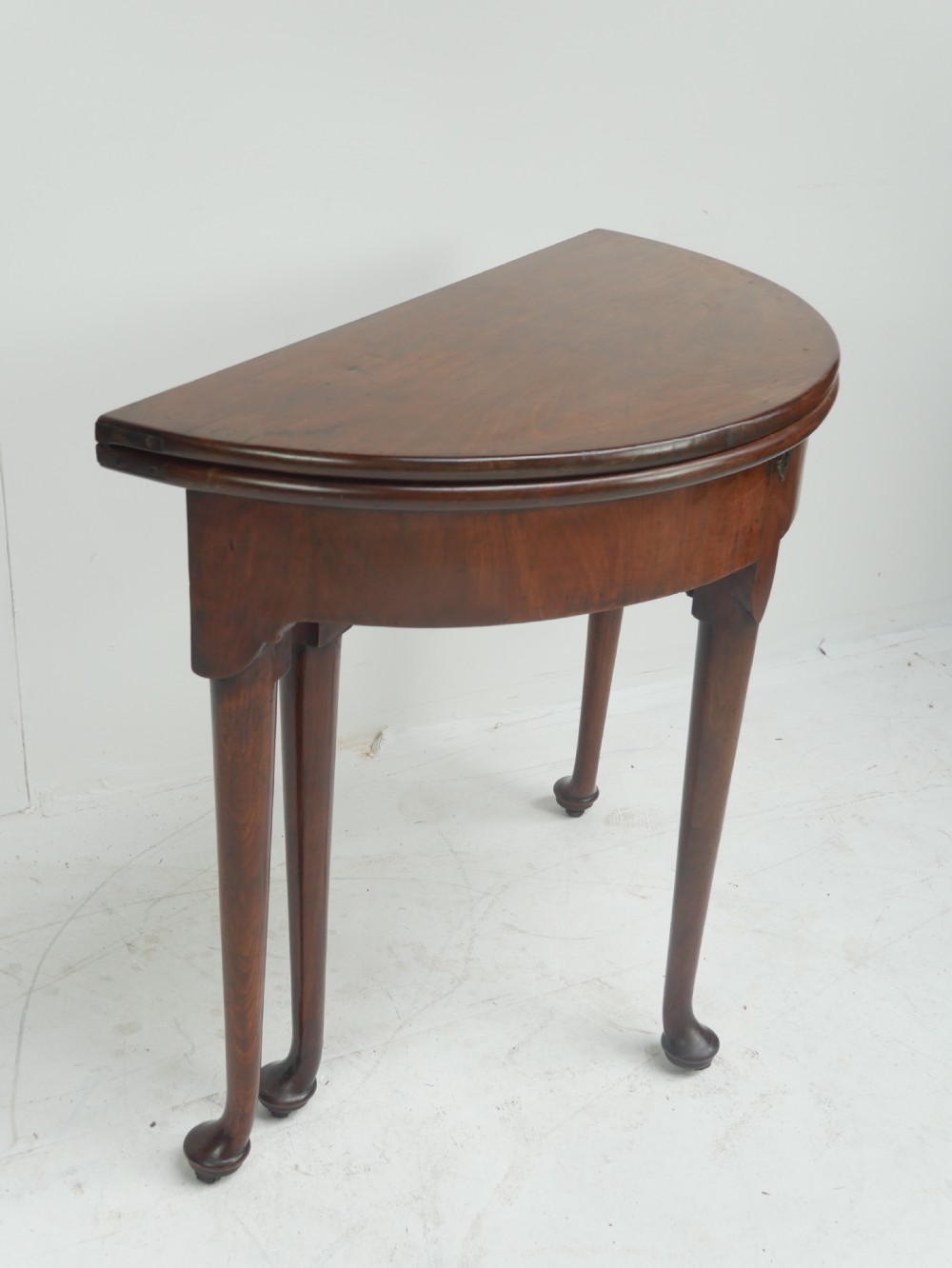 An 18th-century mahogany demi-lune games table featuring a folding semi-circular top supported by slender legs with pad feet.