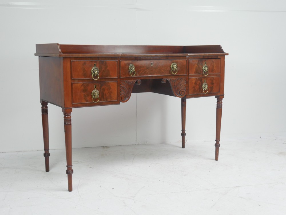 A Regency flame mahogany sideboard featuring five drawers with brass lion mask handles, turned reeded legs, and carved corner brackets.