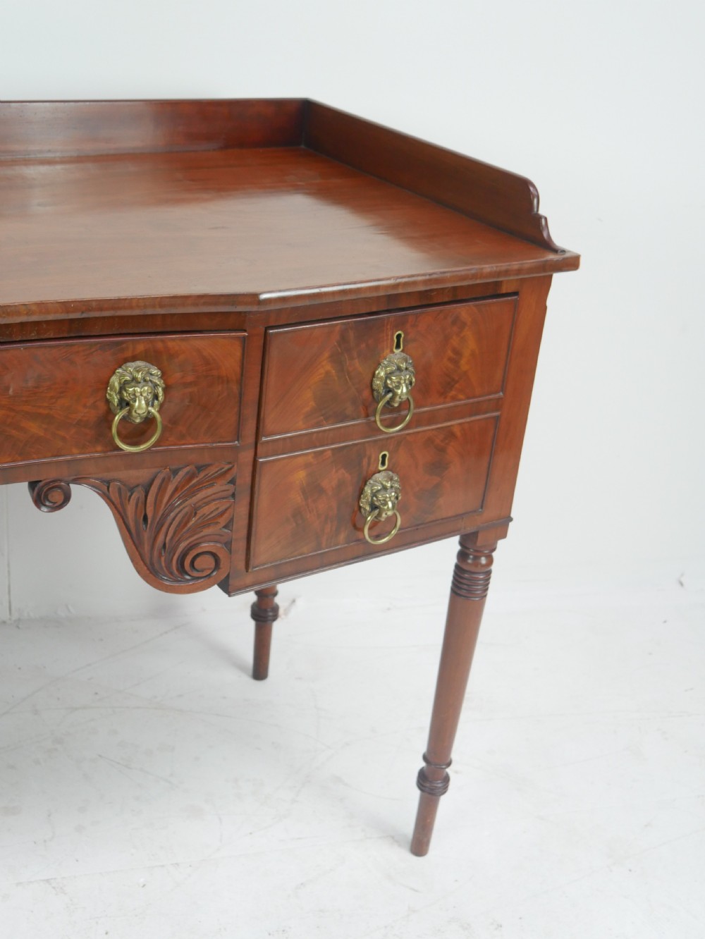 A Regency flame mahogany sideboard featuring five drawers with brass lion mask handles, turned reeded legs, and carved corner brackets. View III