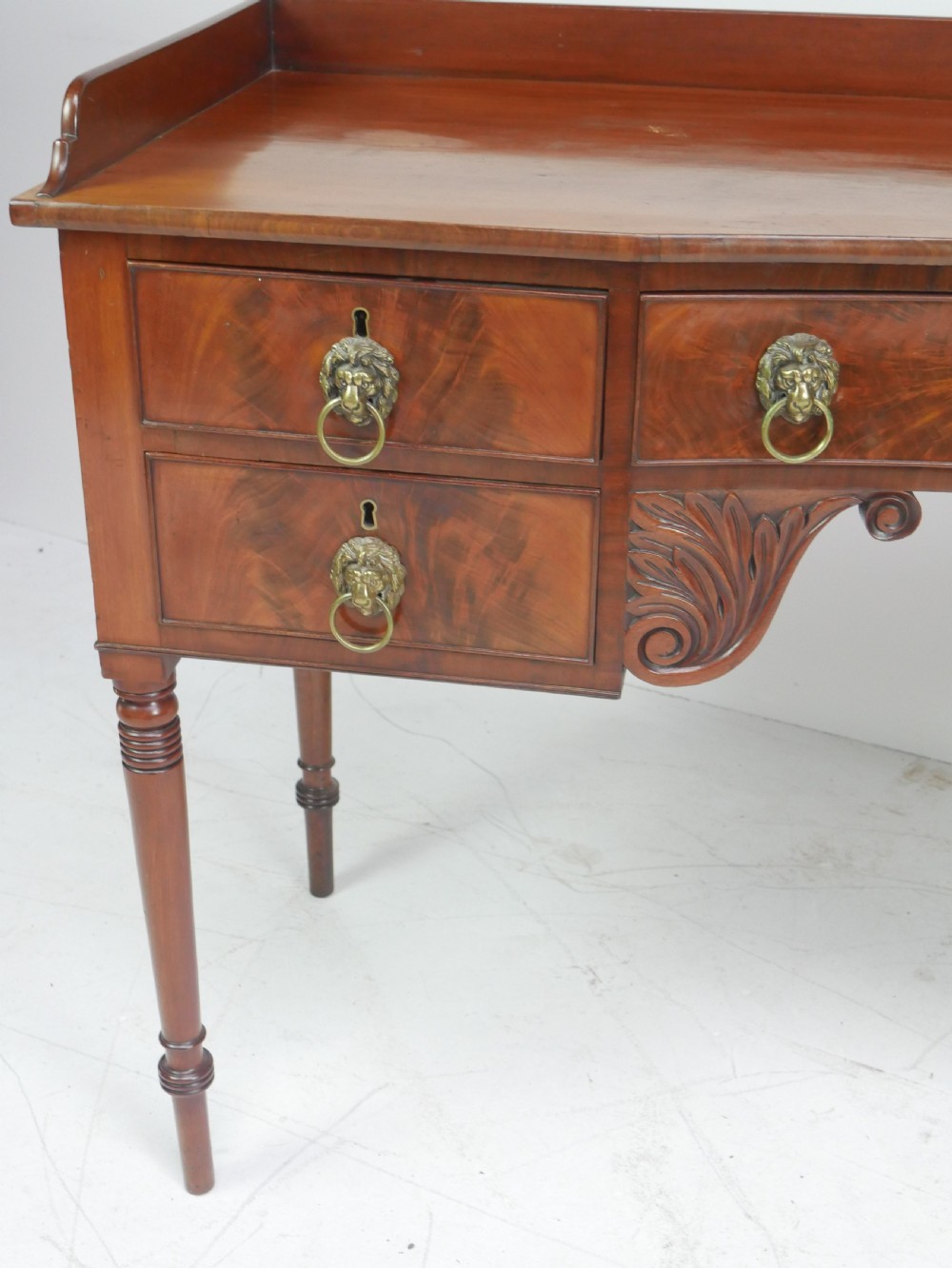 A Regency flame mahogany sideboard featuring five drawers with brass lion mask handles, turned reeded legs, and carved corner brackets. View V