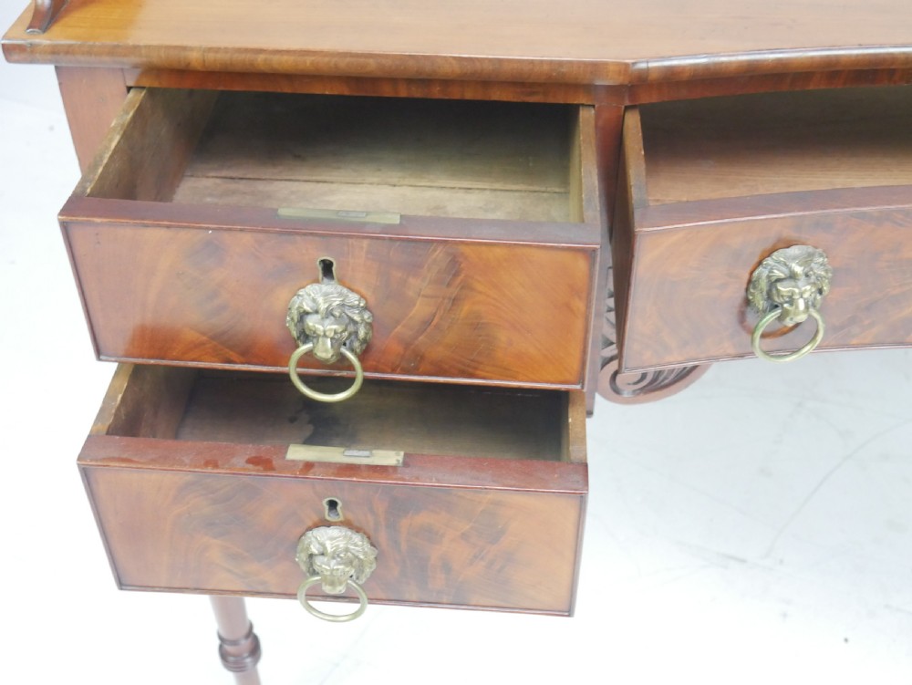A Regency flame mahogany sideboard featuring five drawers with brass lion mask handles, turned reeded legs, and carved corner brackets. View VII