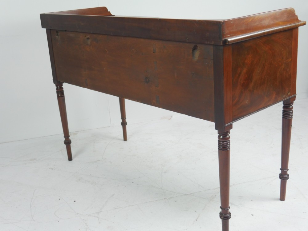 A Regency flame mahogany sideboard featuring five drawers with brass lion mask handles, turned reeded legs, and carved corner brackets. View XVI