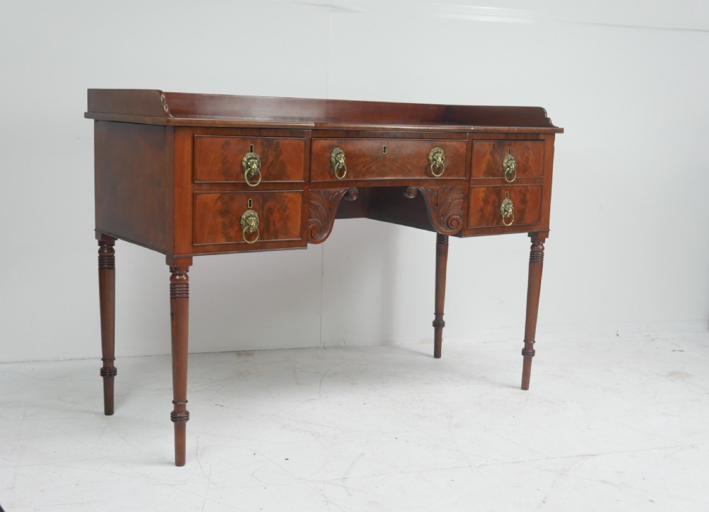 A Regency flame mahogany sideboard featuring five drawers with brass lion mask handles, turned reeded legs, and carved corner brackets. View XVII
