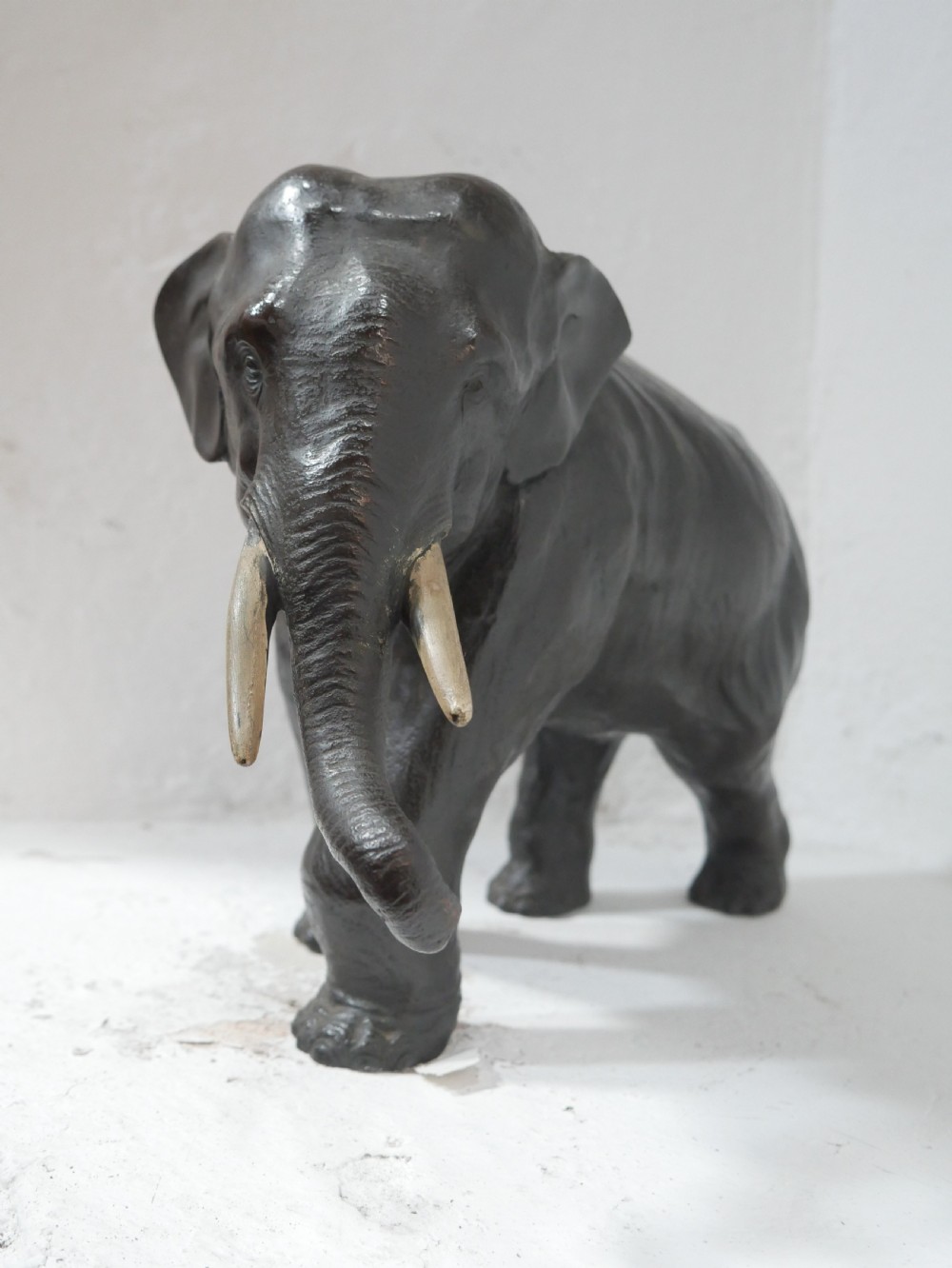 A dark patinated bronze figure of an elephant in mid-stride featuring light-coloured tusks and textured skin detail. View II