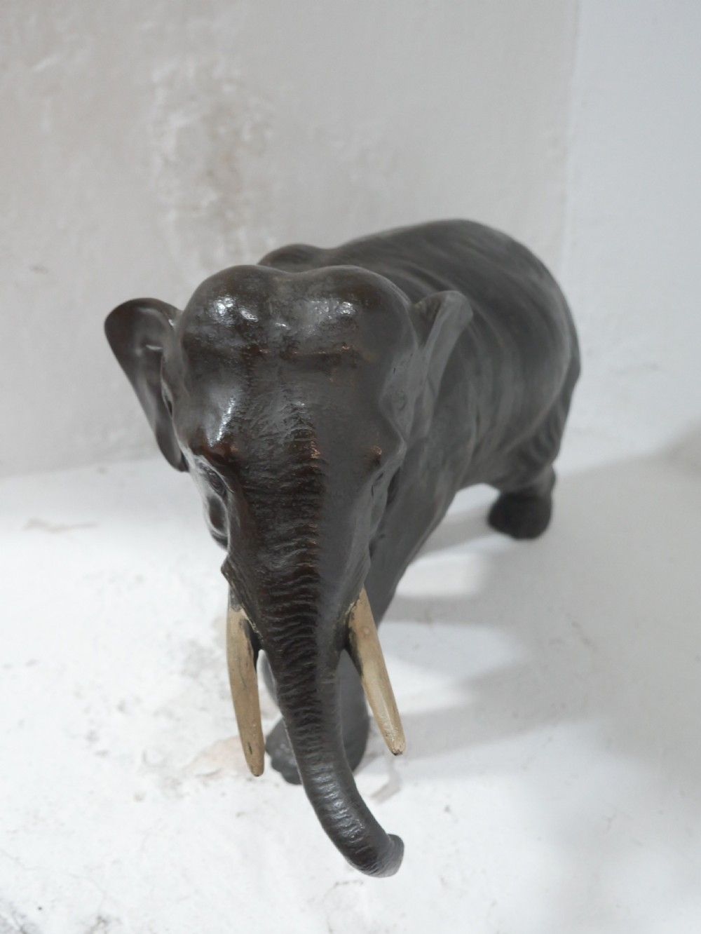 A dark patinated bronze figure of an elephant in mid-stride featuring light-coloured tusks and textured skin detail. View III