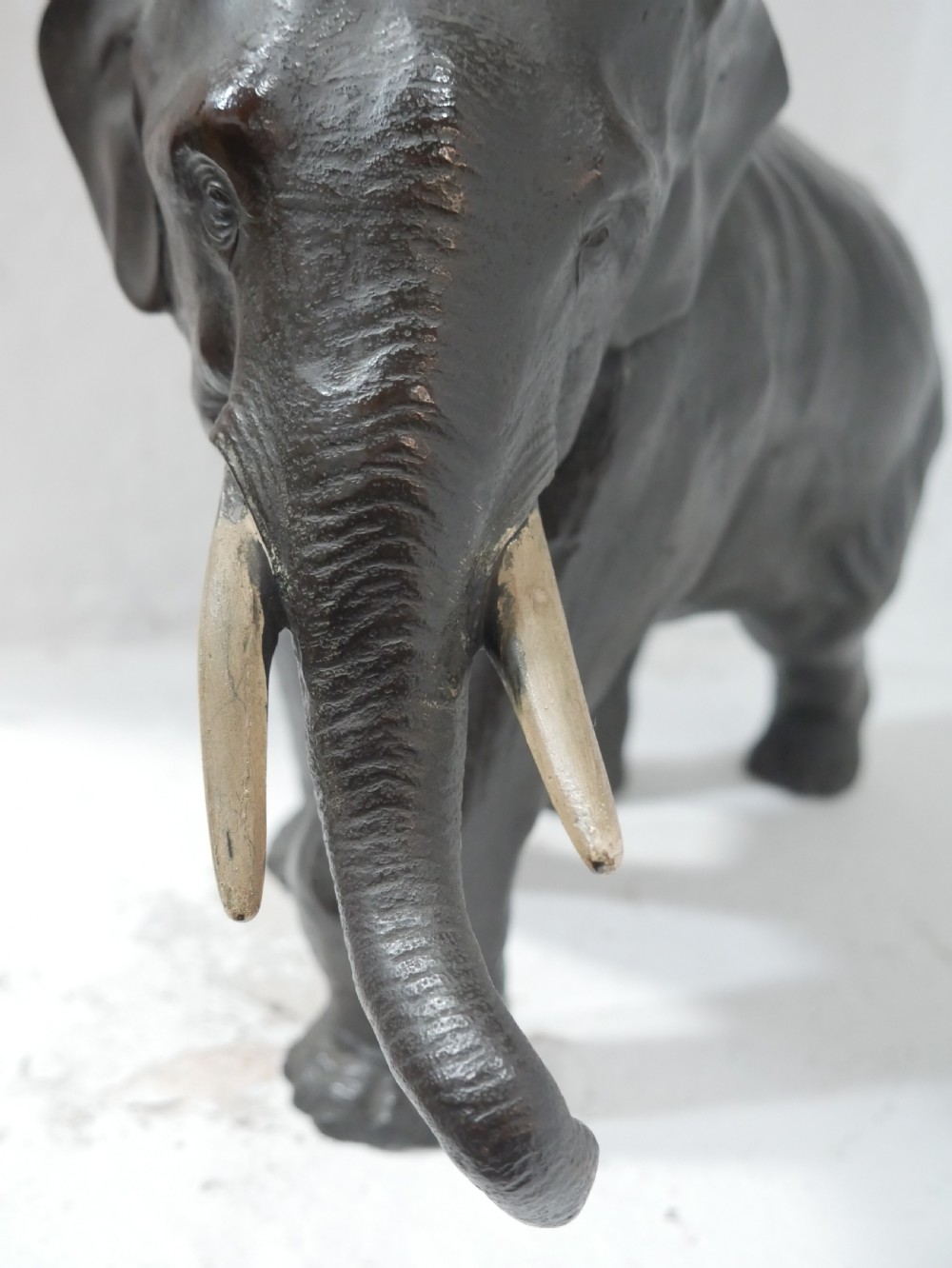 A dark patinated bronze figure of an elephant in mid-stride featuring light-coloured tusks and textured skin detail. View V