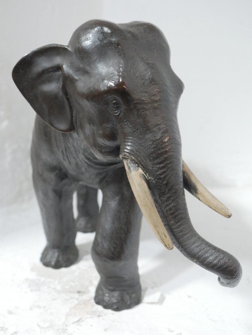 A dark patinated bronze figure of an elephant in mid-stride featuring light-coloured tusks and textured skin detail. View VII