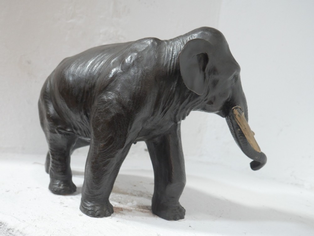 A dark patinated bronze figure of an elephant in mid-stride featuring light-coloured tusks and textured skin detail. View VIII