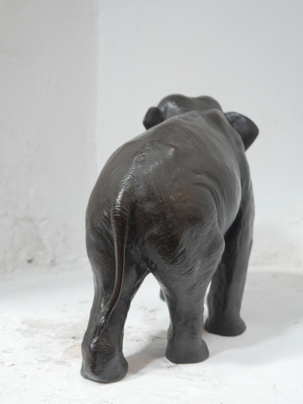 A dark patinated bronze figure of an elephant in mid-stride featuring light-coloured tusks and textured skin detail. View IX