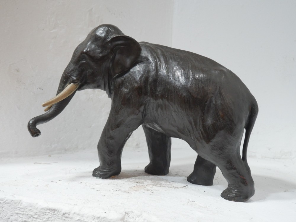 A dark patinated bronze figure of an elephant in mid-stride featuring light-coloured tusks and textured skin detail. View X