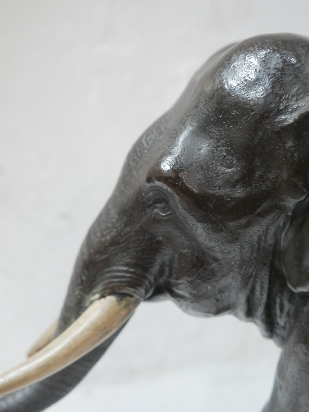 A dark patinated bronze figure of an elephant in mid-stride featuring light-coloured tusks and textured skin detail. View XI