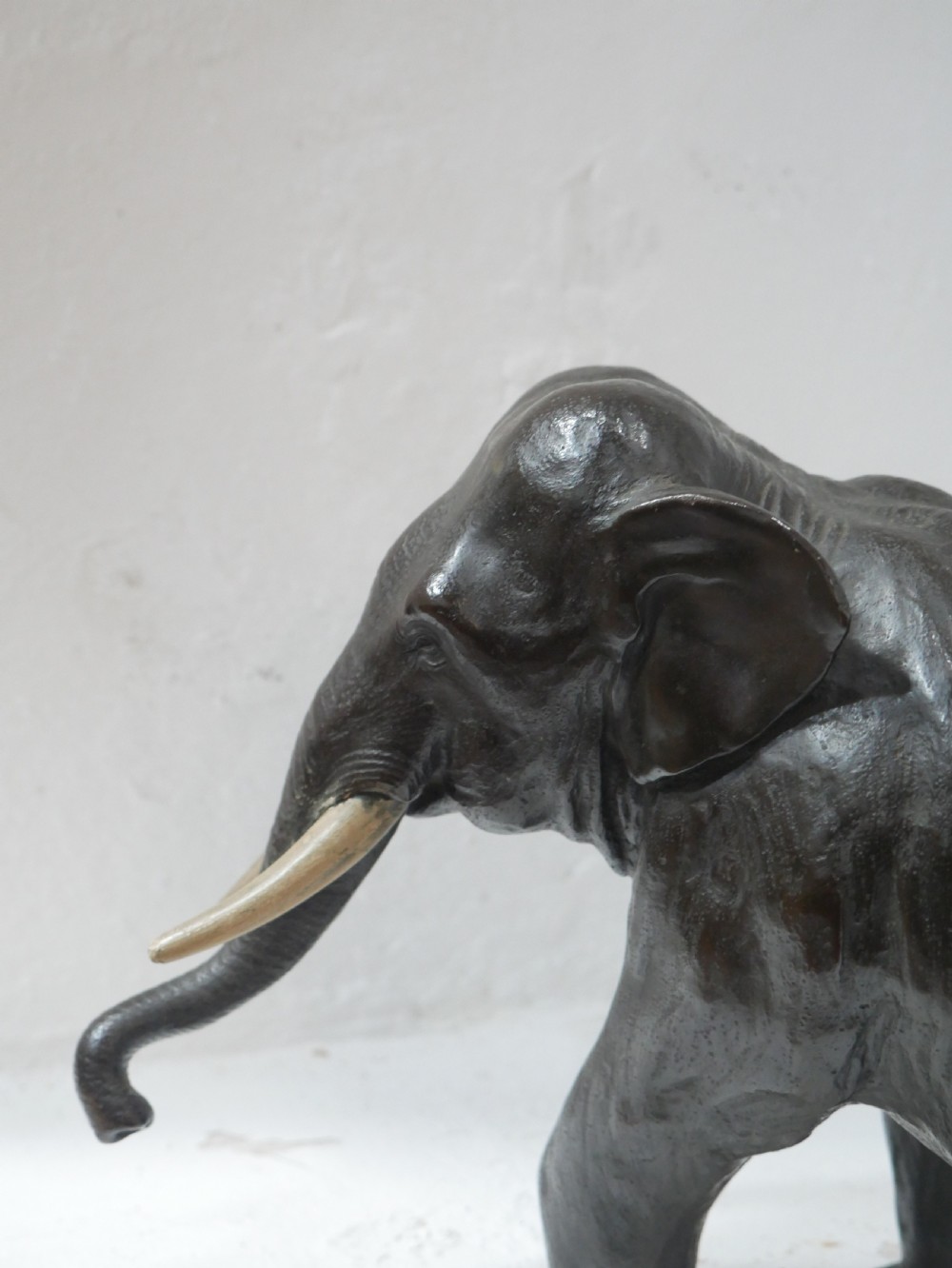 A dark patinated bronze figure of an elephant in mid-stride featuring light-coloured tusks and textured skin detail. View XII