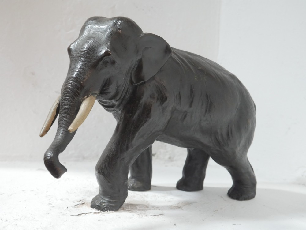 A dark patinated bronze figure of an elephant in mid-stride featuring light-coloured tusks and textured skin detail. View XIV