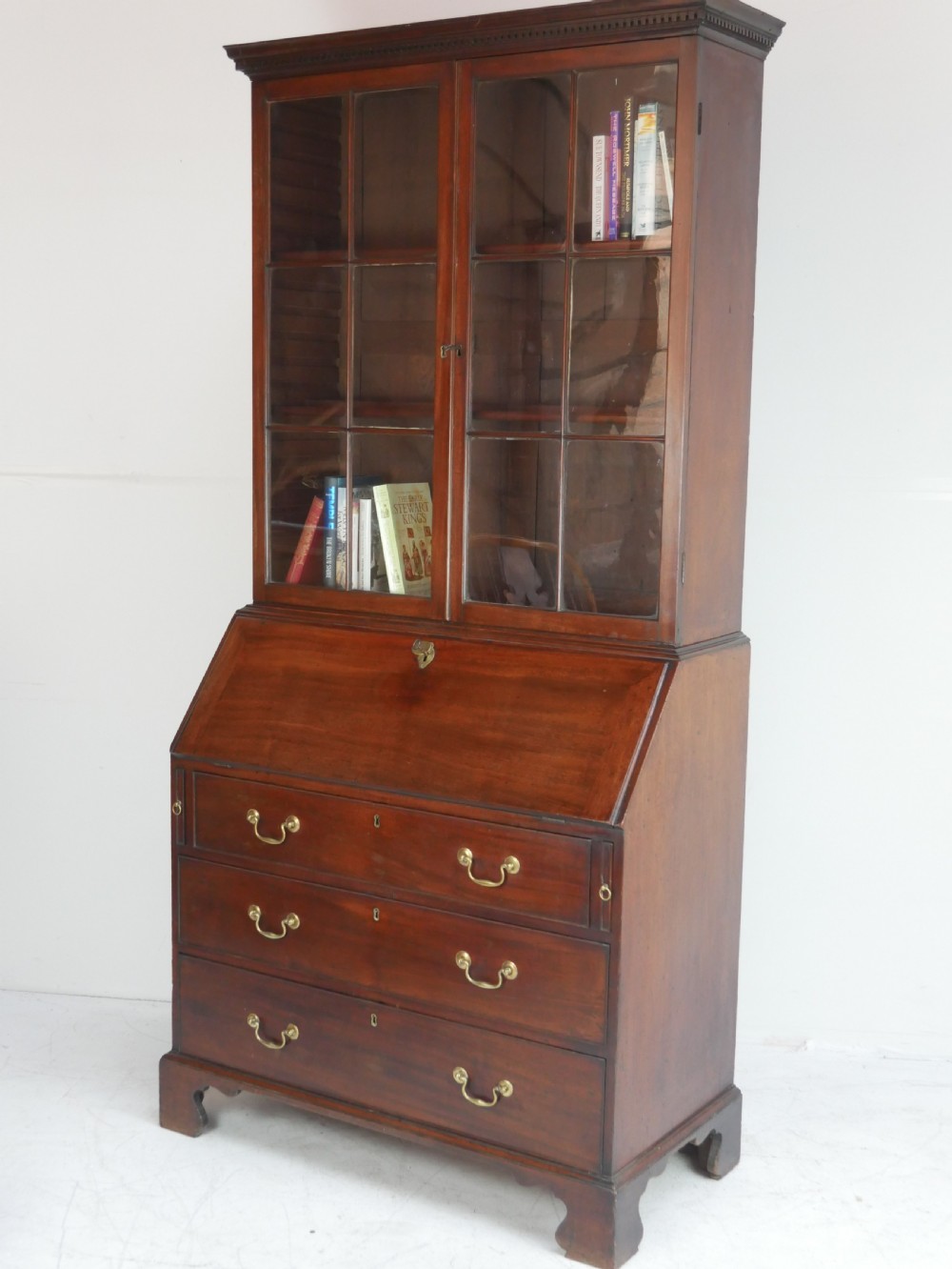 A Georgian mahogany bureau bookcase featuring a two-door glazed upper cabinet, a slant-front writing bureau, and three long drawers with brass handles.