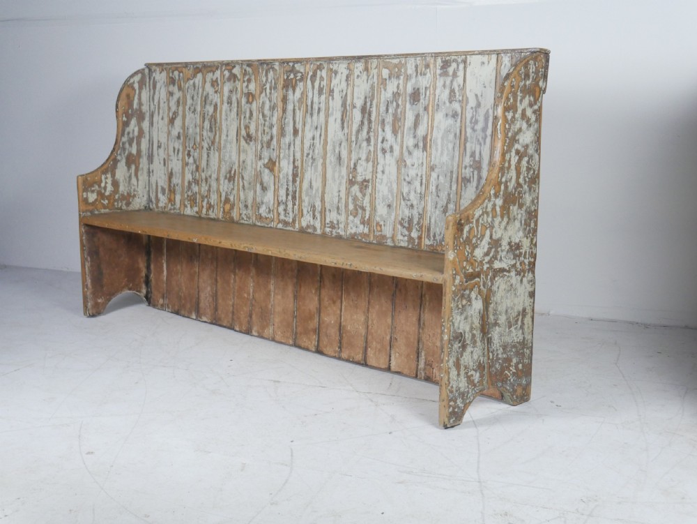 A large high-backed wooden settle bench featuring distressed cream paint over natural wood and vertical panelled detailing.