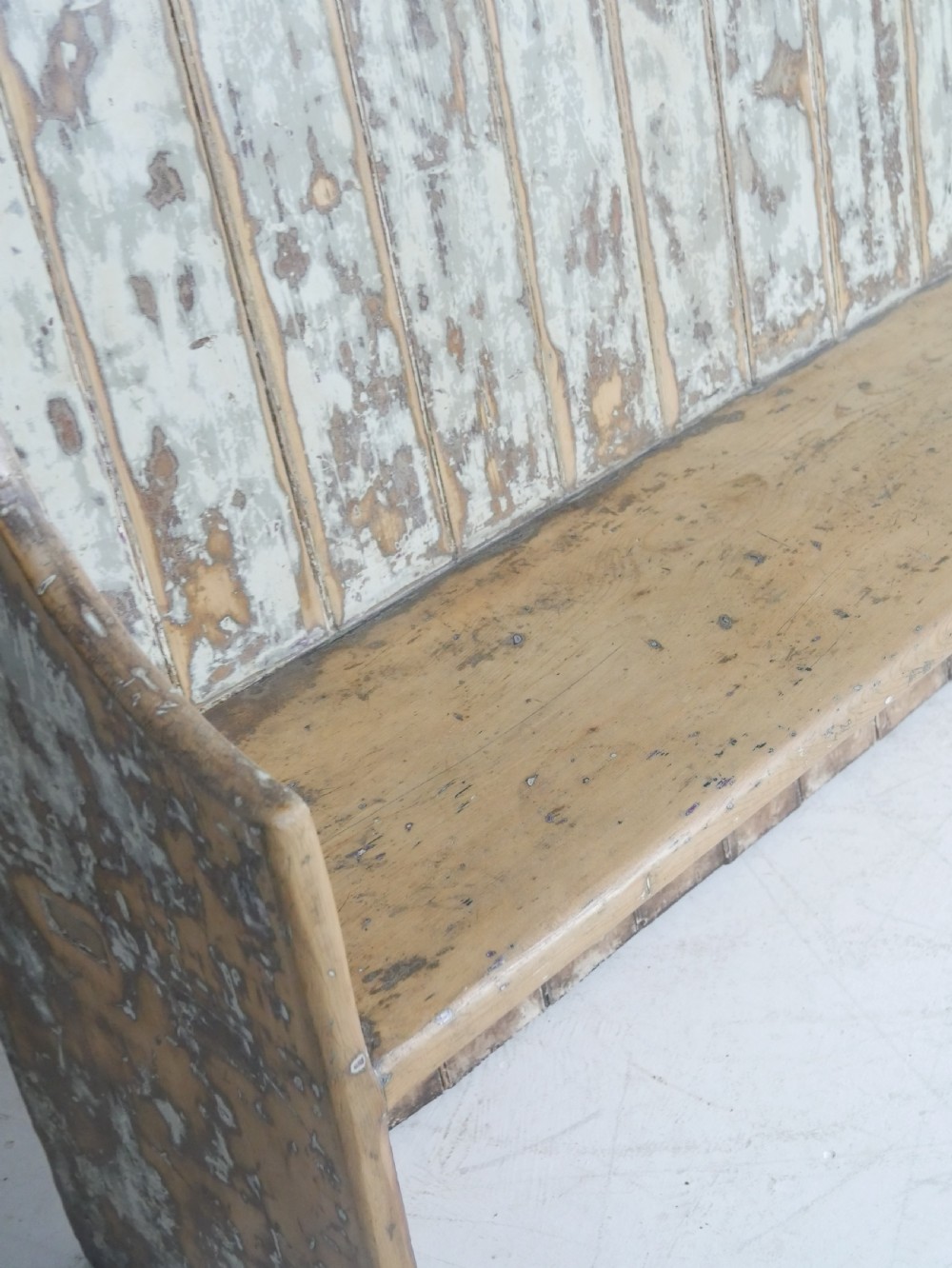 A large high-backed wooden settle bench featuring distressed cream paint over natural wood and vertical panelled detailing. View VI