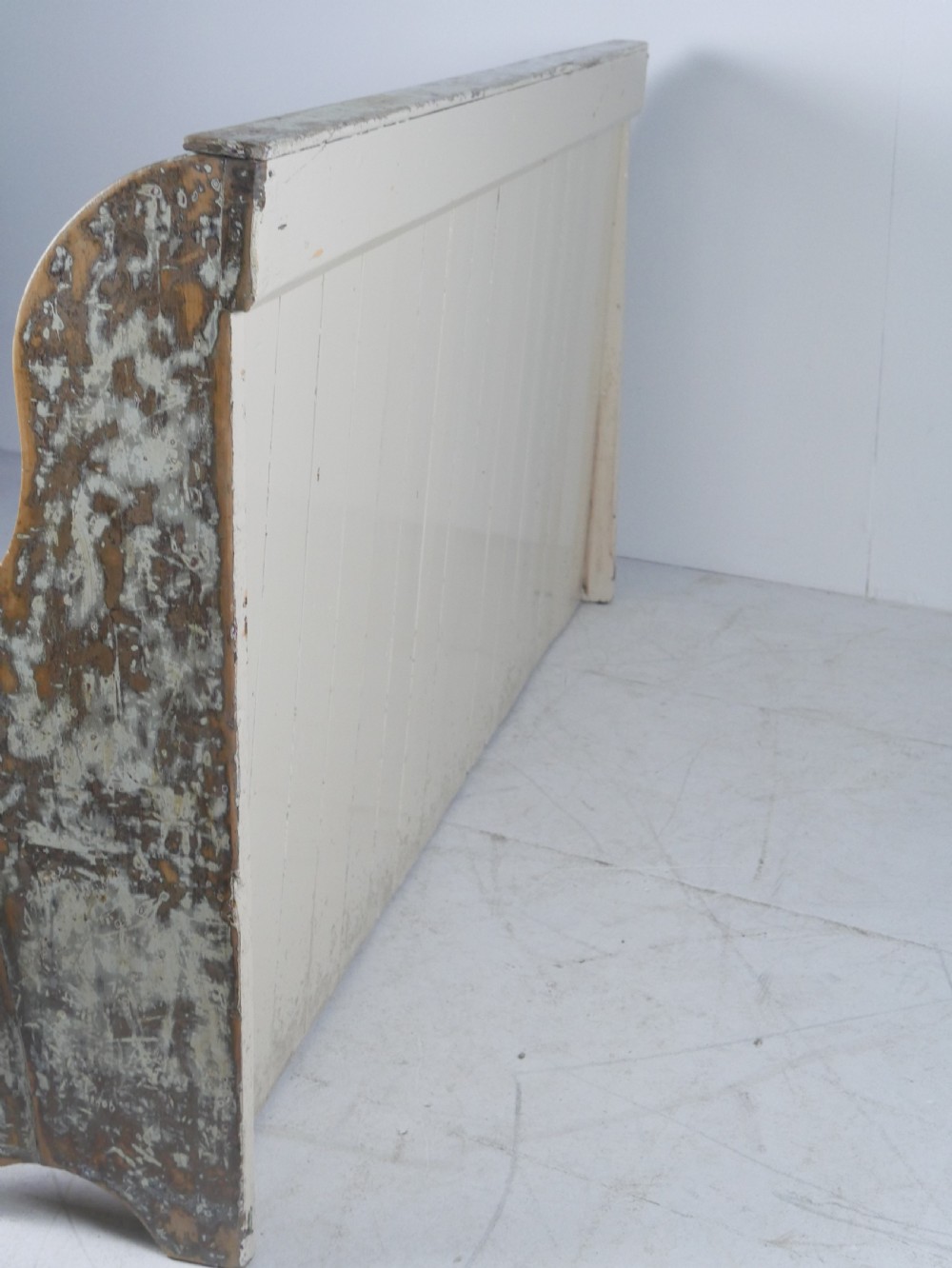 A large high-backed wooden settle bench featuring distressed cream paint over natural wood and vertical panelled detailing. View VII