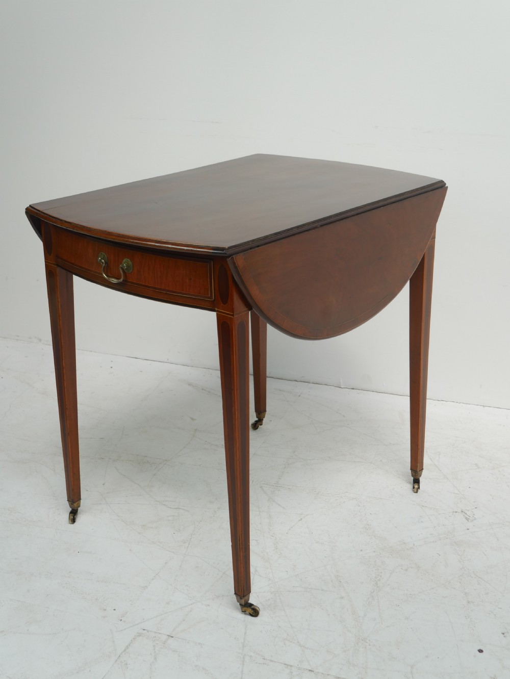A Georgian mahogany Pembroke table featuring two drop leaves, a single drawer with a brass handle, string inlay on square tapered legs, and brass castors.