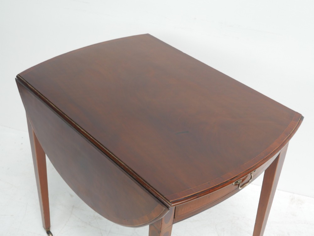 A Georgian mahogany Pembroke table featuring two drop leaves, a single drawer with a brass handle, string inlay on square tapered legs, and brass castors. View VII