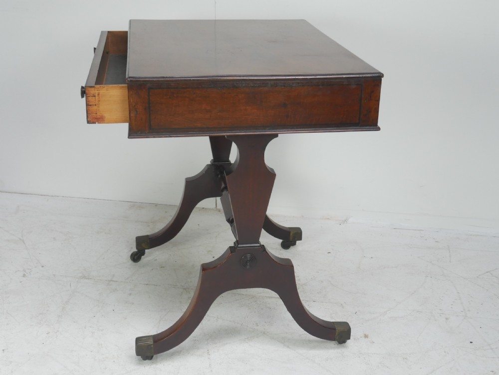A Regency mahogany side table featuring a single drawer with brass knobs, a turned cross stretcher, and splayed legs on castors. View III