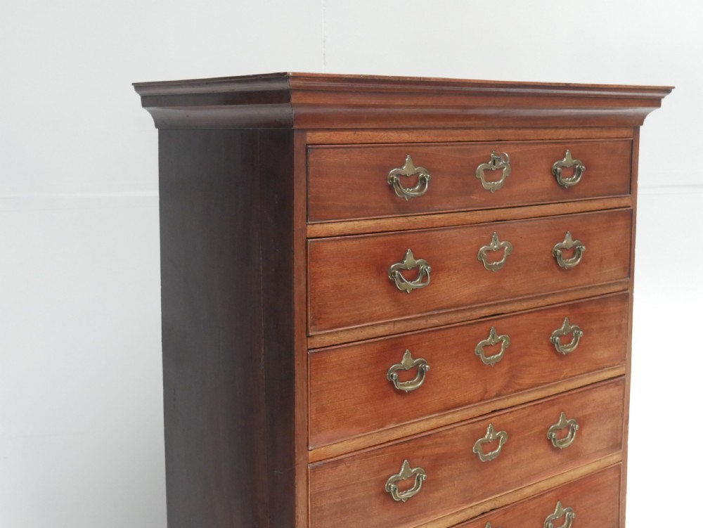 A tall, narrow mahogany chest of drawers featuring seven graduated drawers with brass drop handles and decorative shaped bracket feet. View II