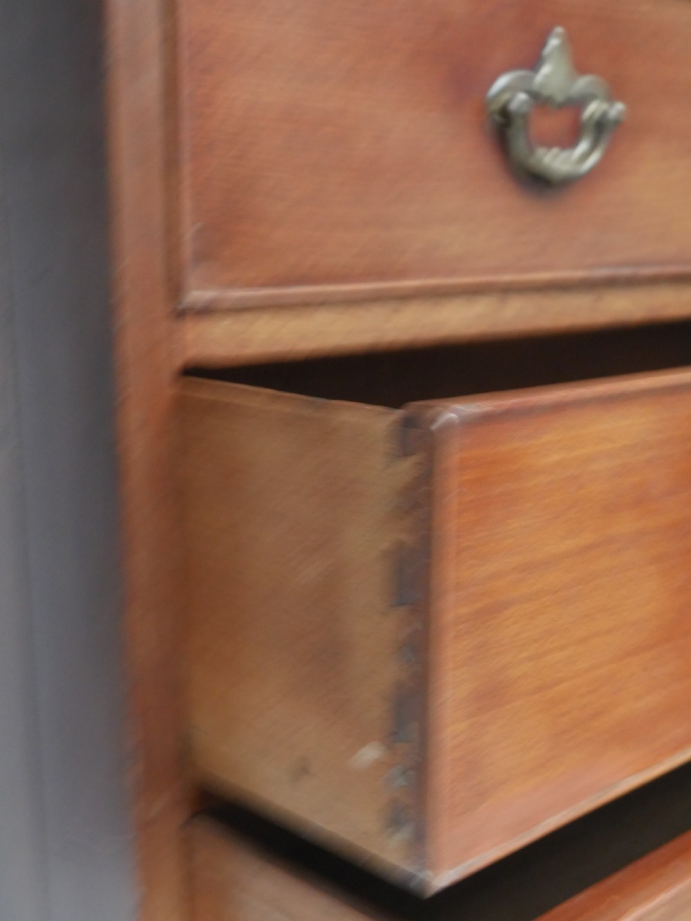 A tall, narrow mahogany chest of drawers featuring seven graduated drawers with brass drop handles and decorative shaped bracket feet. View IX