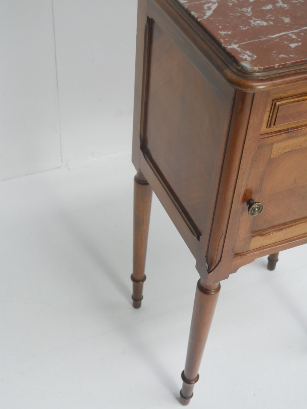 A French provincial walnut bedside cabinet with a red marble top, single drawer, inlaid wooden door, and slender turned legs. View V