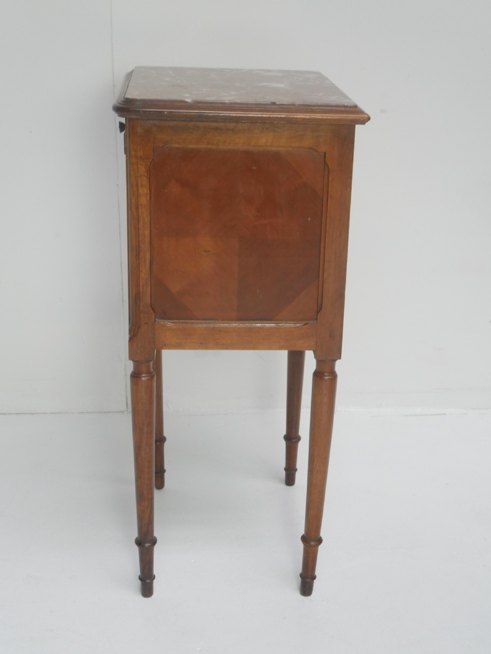 A French provincial walnut bedside cabinet with a red marble top, single drawer, inlaid wooden door, and slender turned legs. View IX