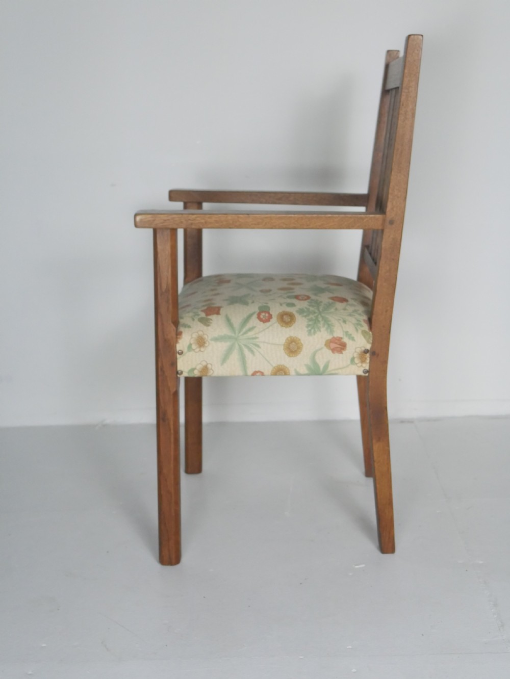 An Arts and Crafts solid oak armchair with a slatted backrest, flat armrests, and a botanical patterned fabric seat secured with studs. View VII