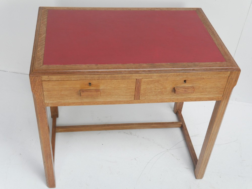 A light oak childs writing desk featuring a red inset leather top, two drawers with wooden pulls, and a square-section frame with a low floor stretcher. View II