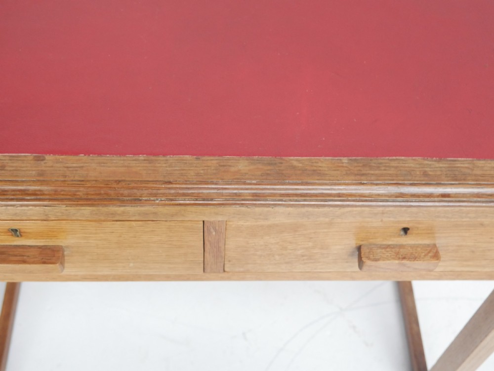 A light oak childs writing desk featuring a red inset leather top, two drawers with wooden pulls, and a square-section frame with a low floor stretcher. View III