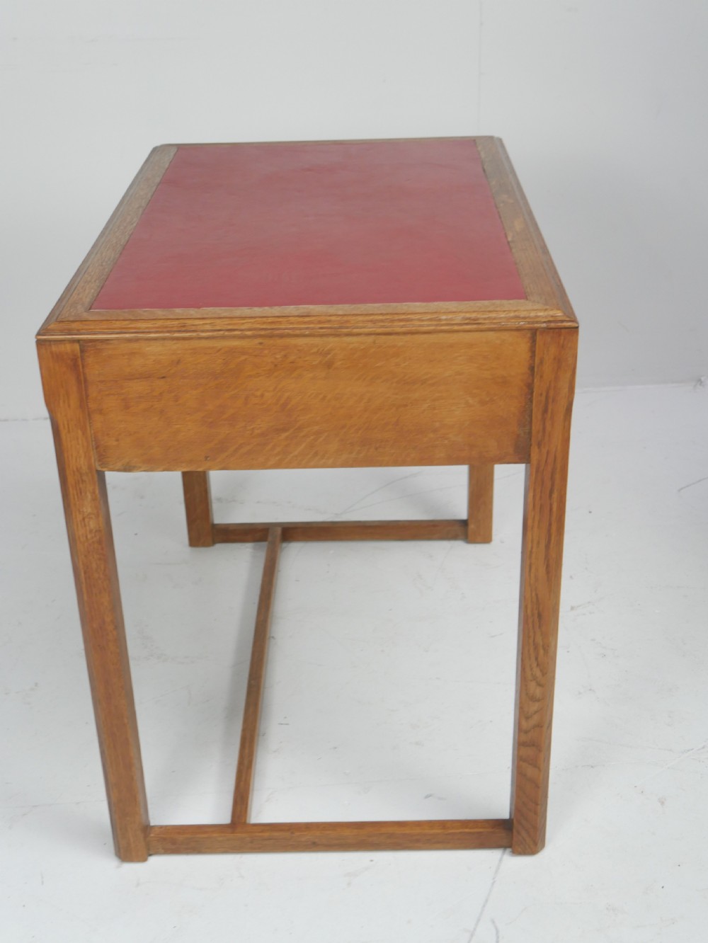 A light oak childs writing desk featuring a red inset leather top, two drawers with wooden pulls, and a square-section frame with a low floor stretcher. View V