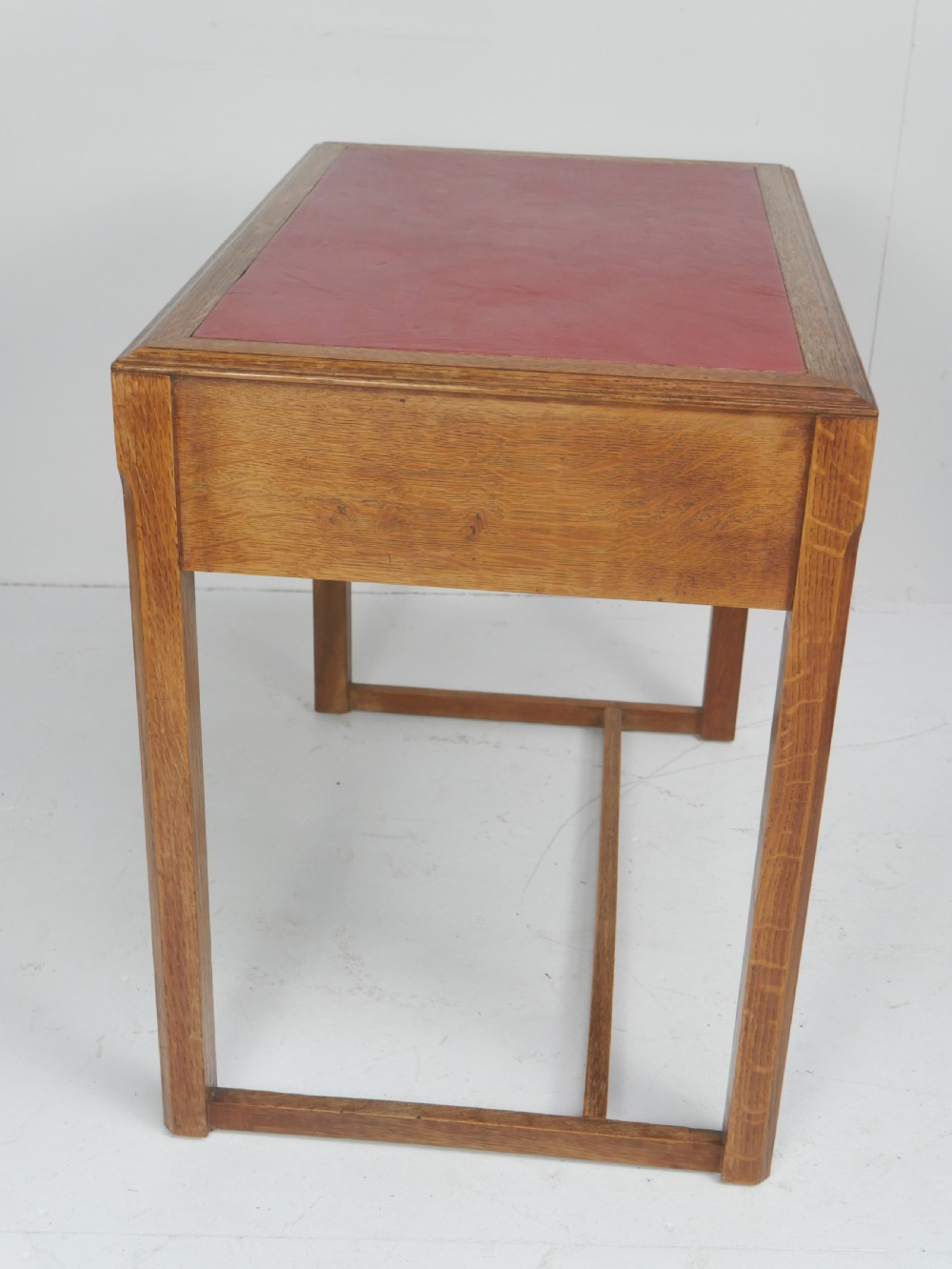 A light oak childs writing desk featuring a red inset leather top, two drawers with wooden pulls, and a square-section frame with a low floor stretcher. View VII