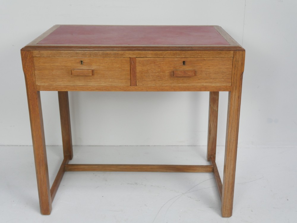 A light oak childs writing desk featuring a red inset leather top, two drawers with wooden pulls, and a square-section frame with a low floor stretcher. View VIII