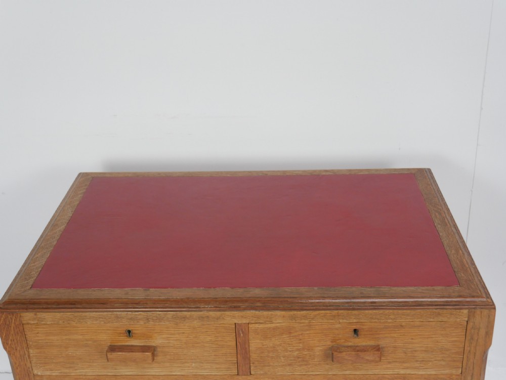 A light oak childs writing desk featuring a red inset leather top, two drawers with wooden pulls, and a square-section frame with a low floor stretcher. View IX