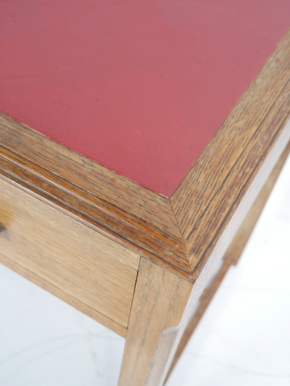A light oak childs writing desk featuring a red inset leather top, two drawers with wooden pulls, and a square-section frame with a low floor stretcher. View X