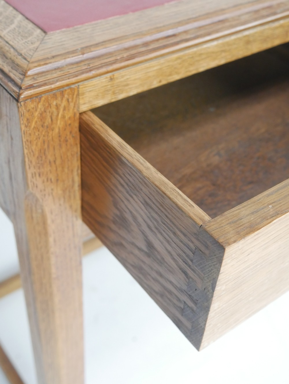A light oak childs writing desk featuring a red inset leather top, two drawers with wooden pulls, and a square-section frame with a low floor stretcher. View XIII