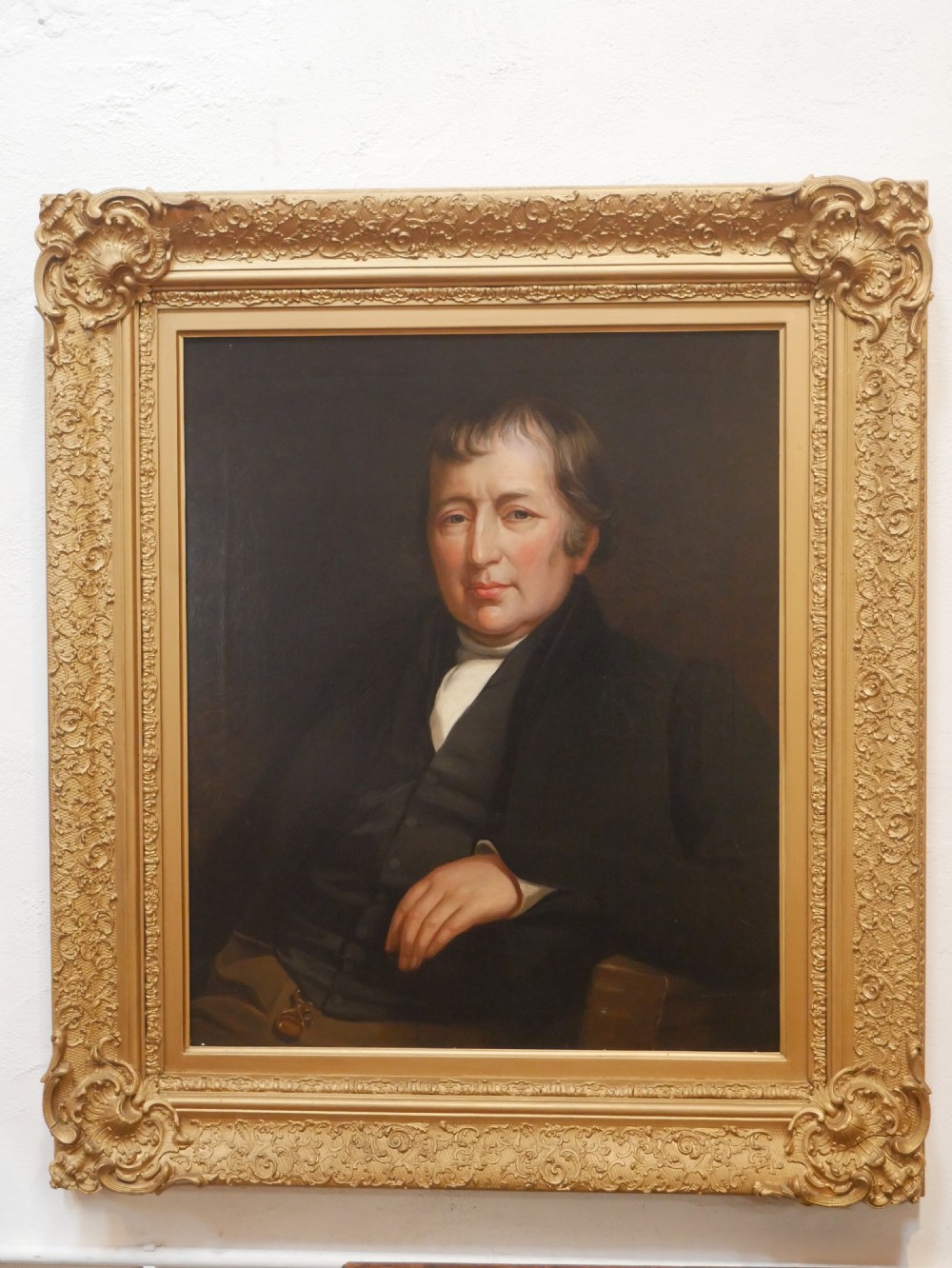 A 19th-century oil painting depicting a gentleman in formal dark attire, framed within an elaborate gold gilt frame. View XV