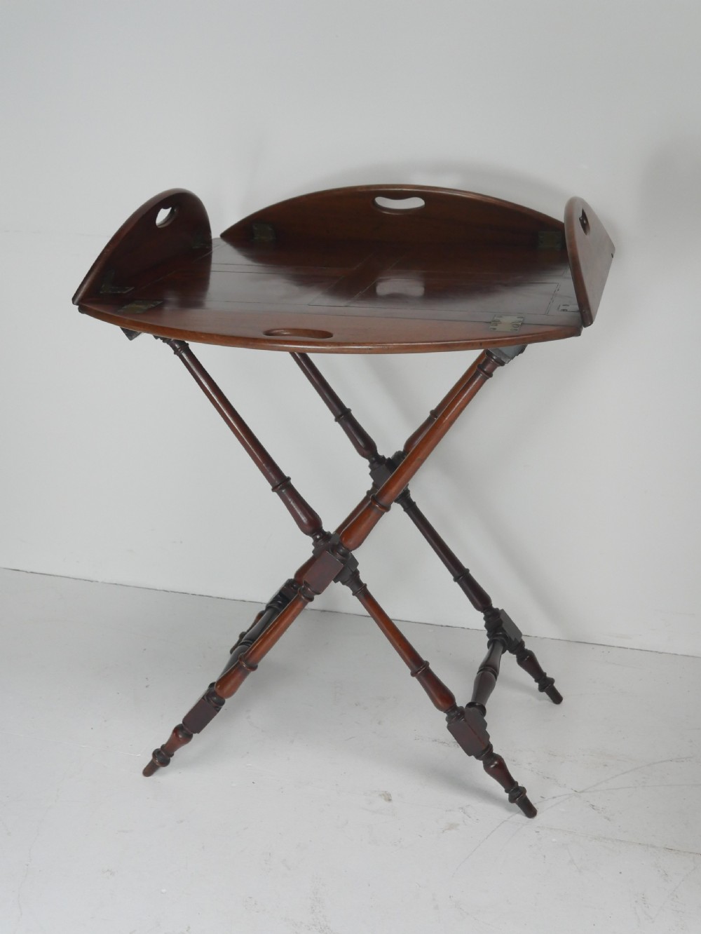 A Regency mahogany butlers tray featuring cutout handles and hinged sides resting on a turned folding X-frame stand.