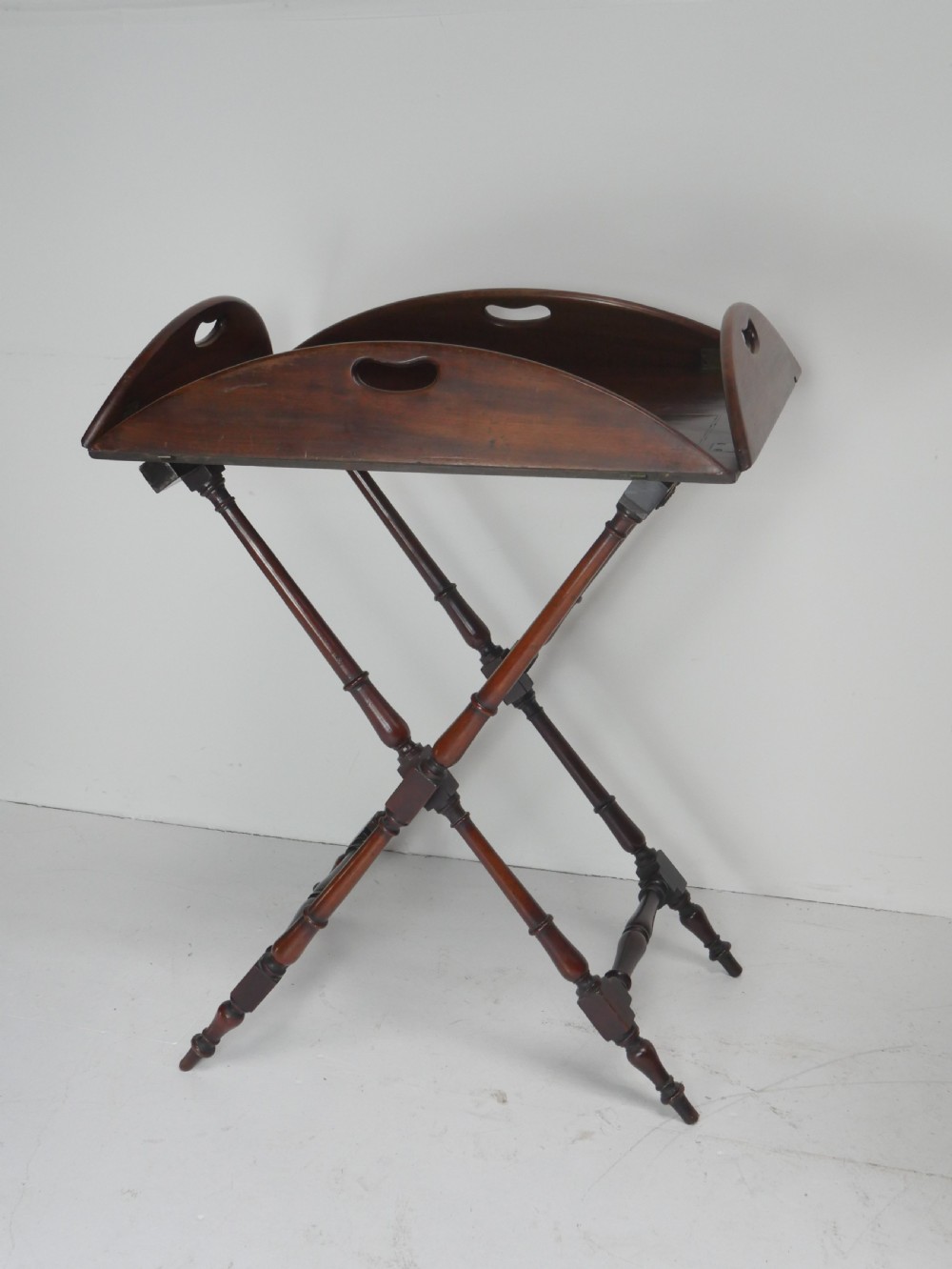 A Regency mahogany butlers tray featuring cutout handles and hinged sides resting on a turned folding X-frame stand. View III