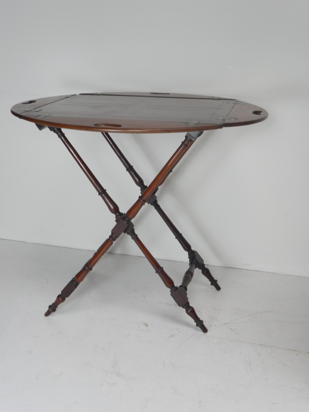 A Regency mahogany butlers tray featuring cutout handles and hinged sides resting on a turned folding X-frame stand. View IX