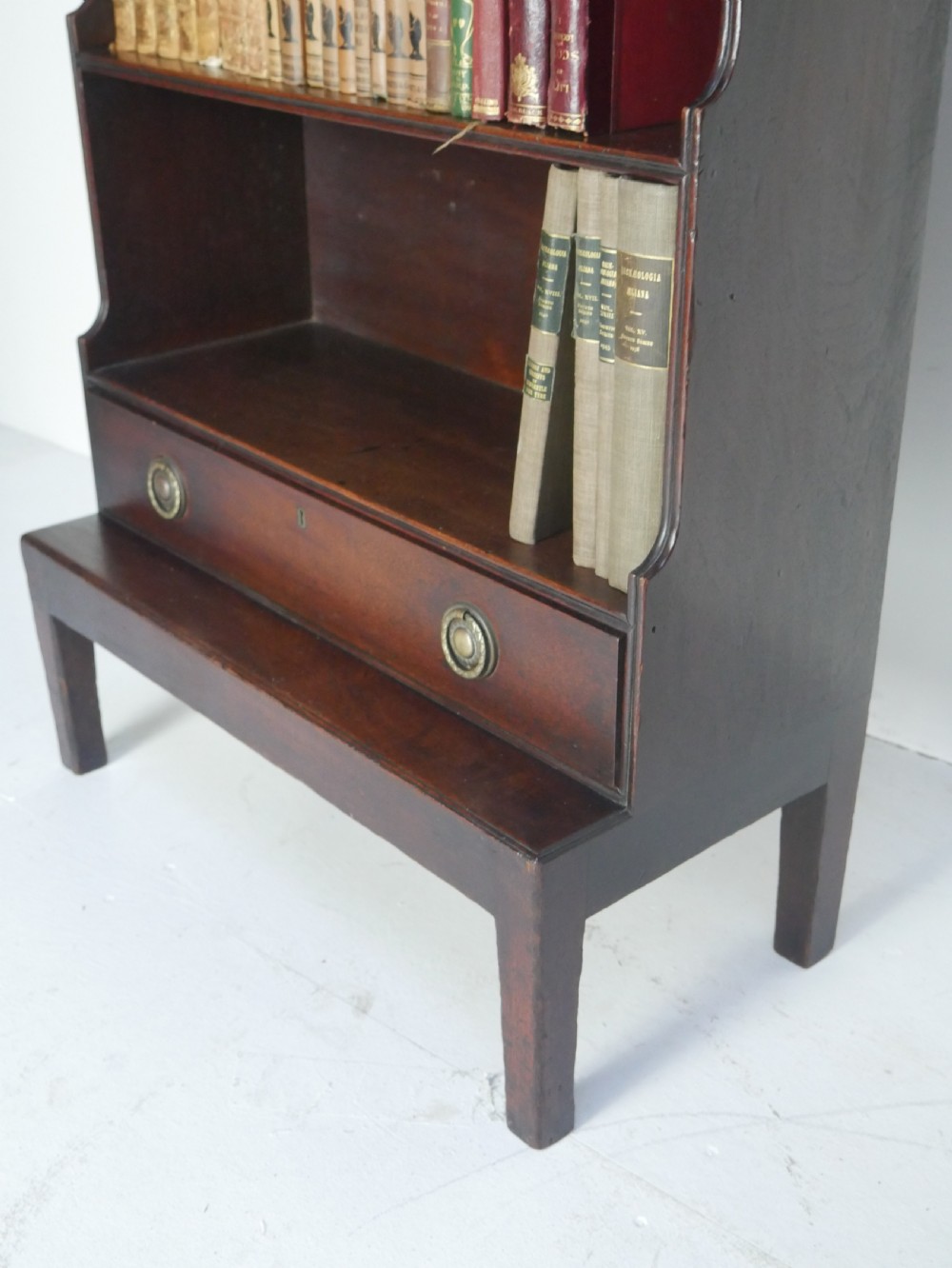 A dark mahogany Georgian waterfall bookcase featuring three open graduated shelves above a single drawer with brass handles. View II