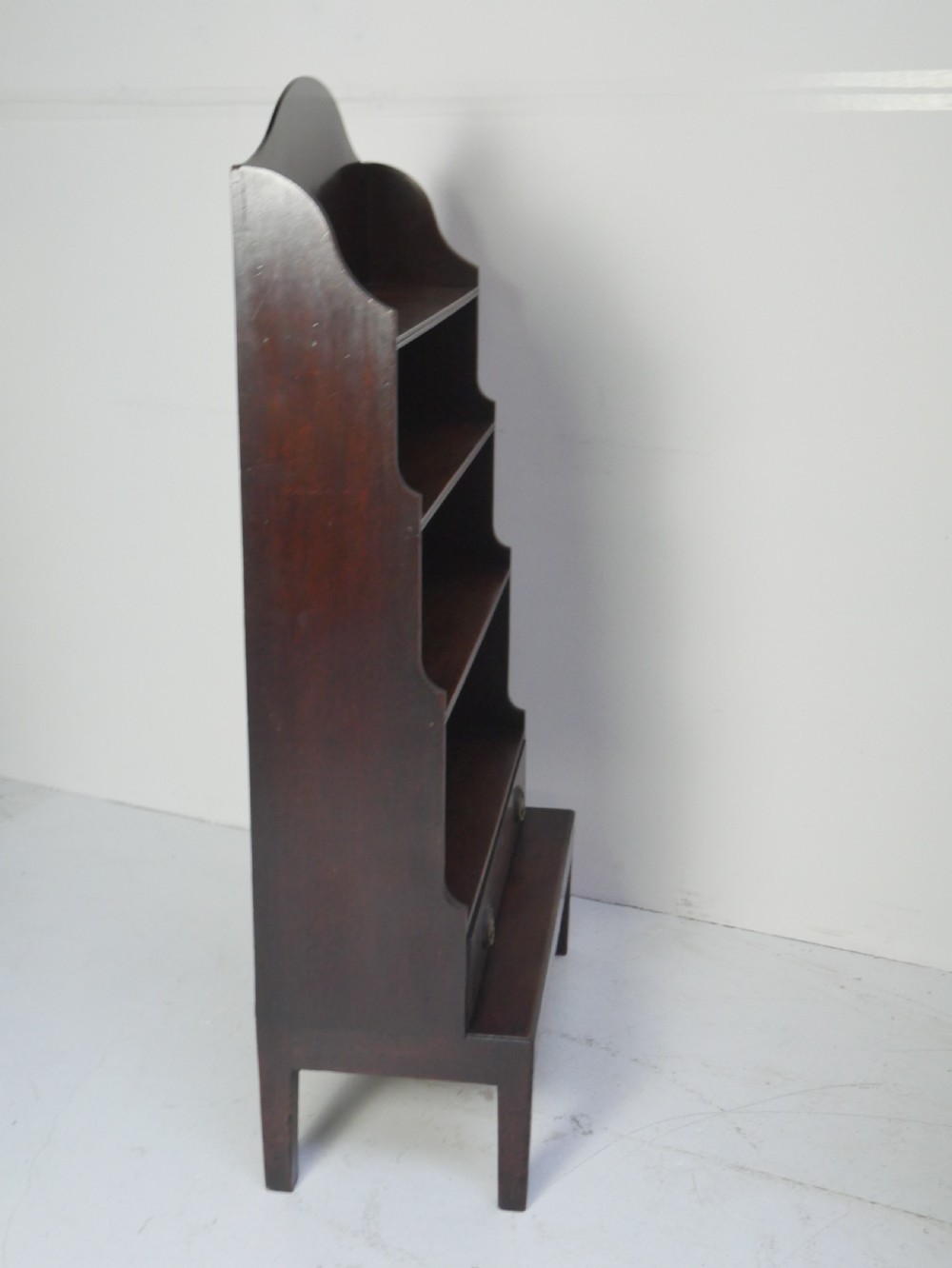 A dark mahogany Georgian waterfall bookcase featuring three open graduated shelves above a single drawer with brass handles. View VII