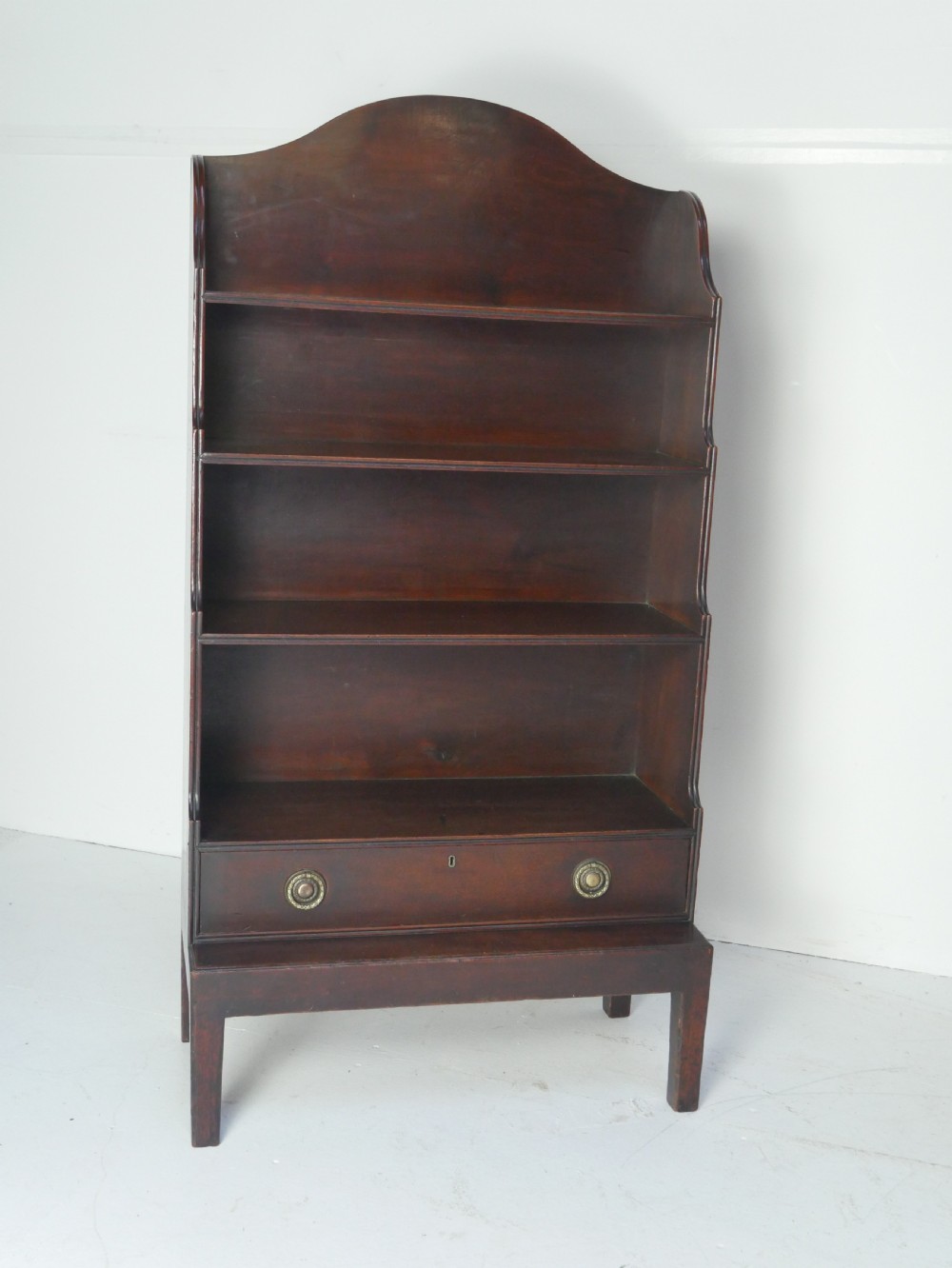 A dark mahogany Georgian waterfall bookcase featuring three open graduated shelves above a single drawer with brass handles. View VIII