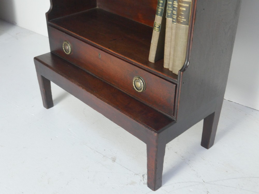 A dark mahogany Georgian waterfall bookcase featuring three open graduated shelves above a single drawer with brass handles. View X