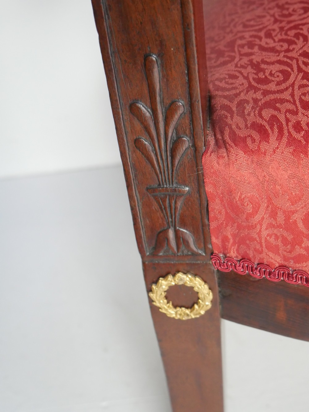 A French Empire style mahogany armchair featuring red damask fabric upholstery, carved armrests, and decorative gilded bronze mounts. View V