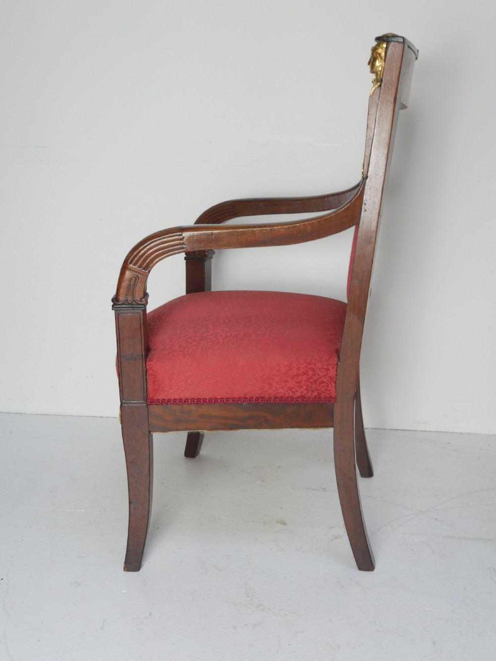 A French Empire style mahogany armchair featuring red damask fabric upholstery, carved armrests, and decorative gilded bronze mounts. View VIII